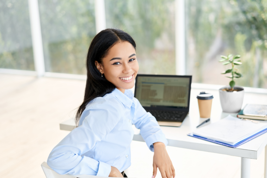 Woman dressed in professional business attire sitting at a desk turned to face a camera behind her